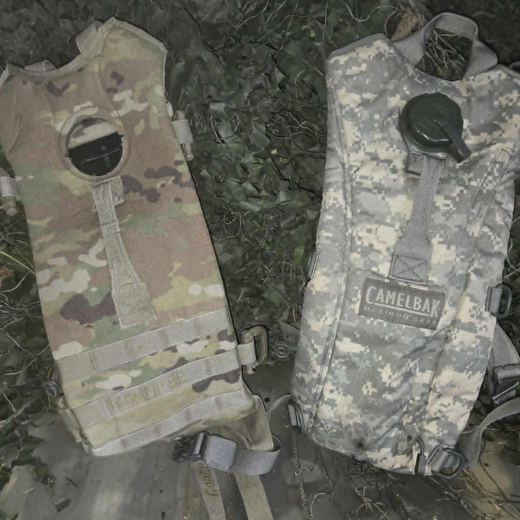 Two camouflage hydration bladders on a grassy background
